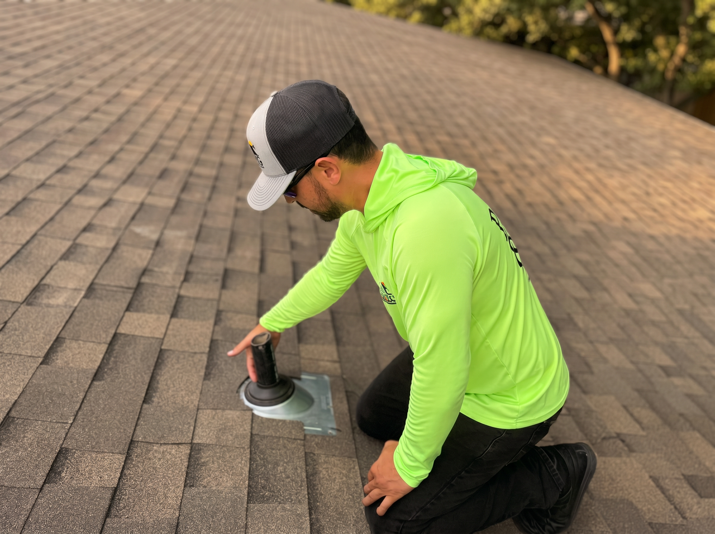 P91 roofer in a bright yellow P91 shirt kneeling on a roof, inspecting a vent boot